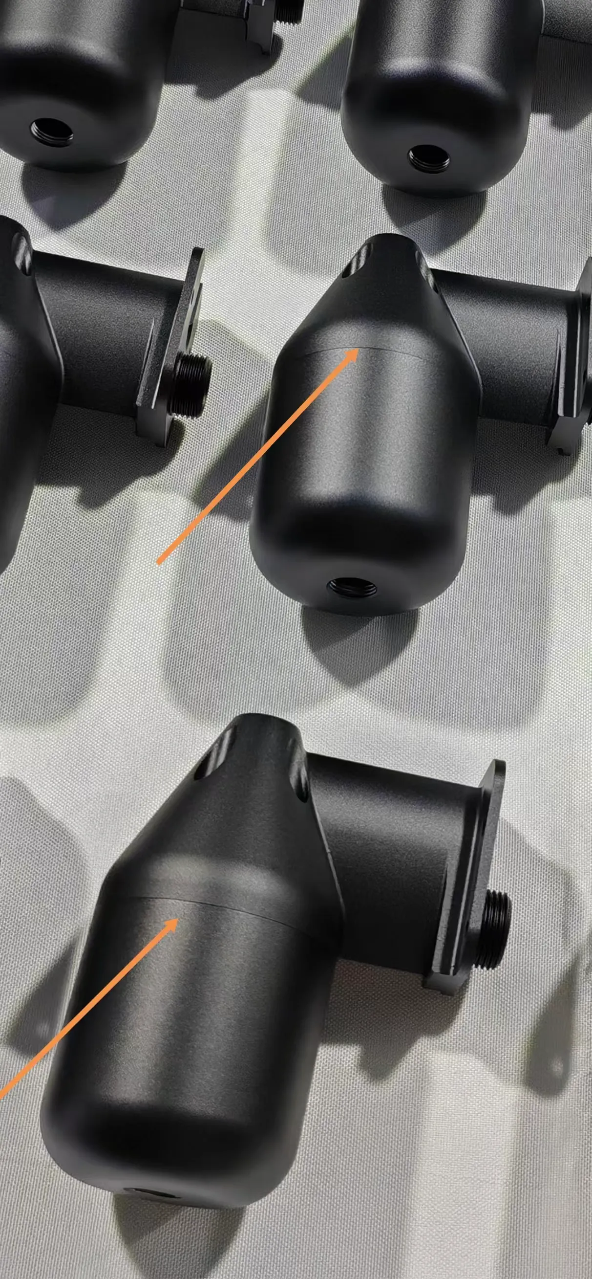 Orange arrows identify the fine curved mating seams between two separate black CNC-machined components