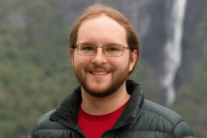 Retrato fotográfico de um diretor de projetos sorridente, de óculos e barba.