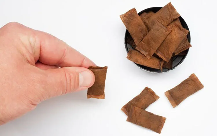 Hand holding nicotine pouches beside an open metal snuff box and snuff can, illustrating modern snus packaging design.
